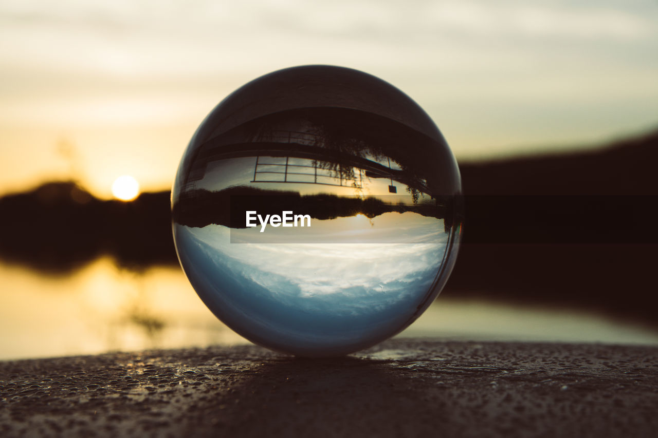 CLOSE-UP OF CRYSTAL BALL ON GLASS AGAINST SUNSET