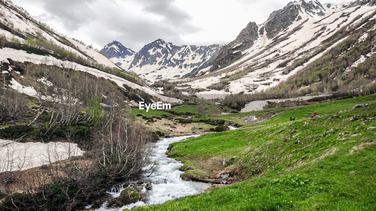 Scenic view of stream amidst snowcapped mountains against sky