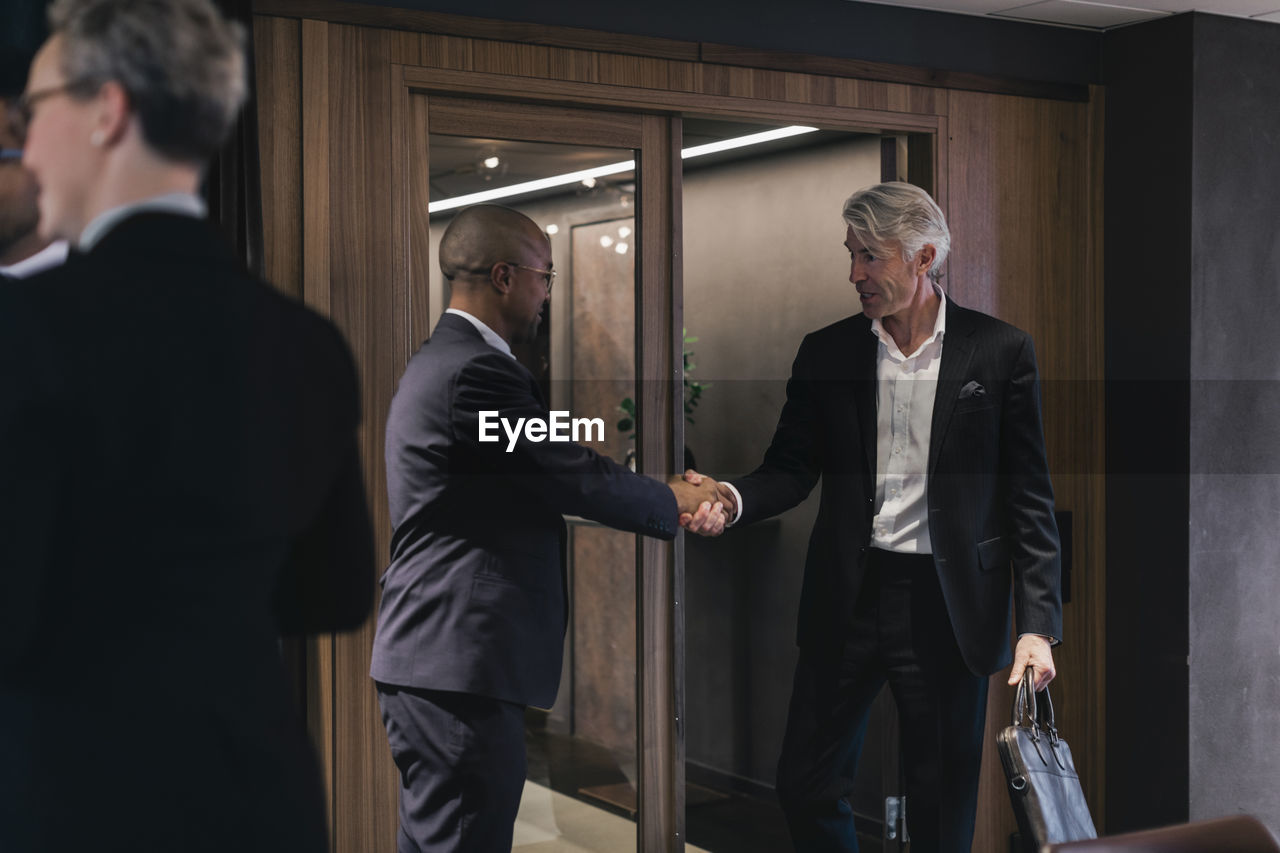 Senior businessman shaking hands with male professional in board room during meeting