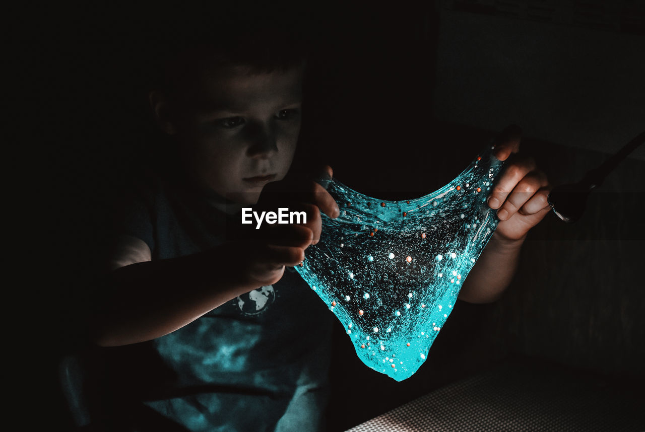 Portrait of boy holding slime in dark room