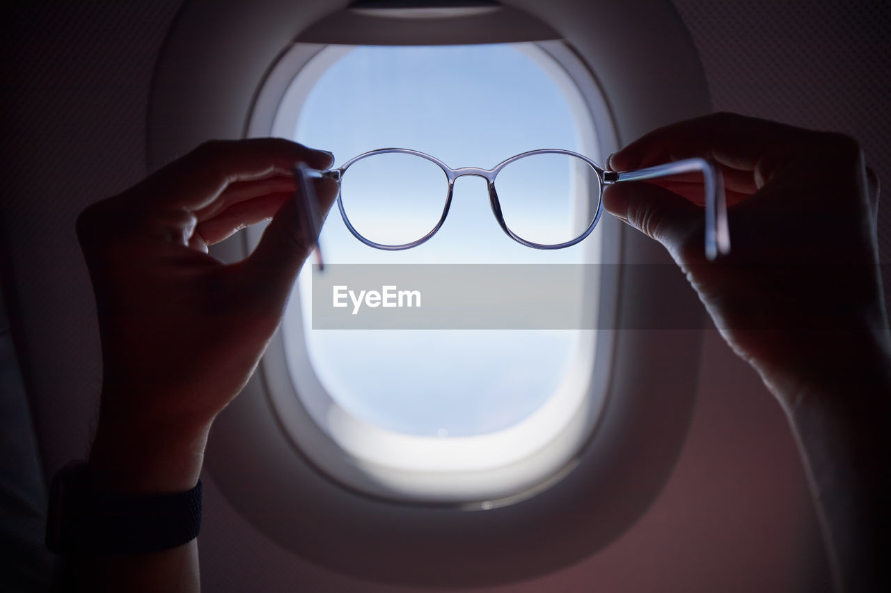 Hand of passenger holding eyeglasses against airplane window during flight. 