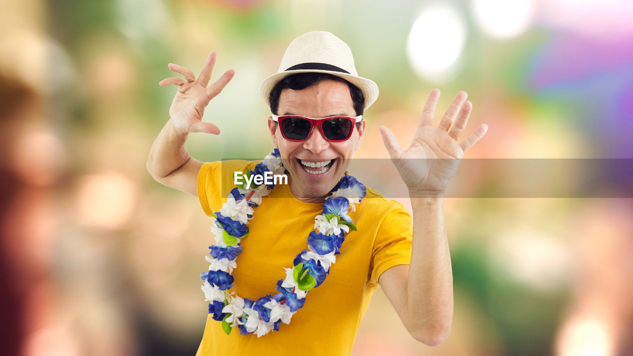 Portrait of excited man wearing sunglasses and floral garland while screaming against colored background