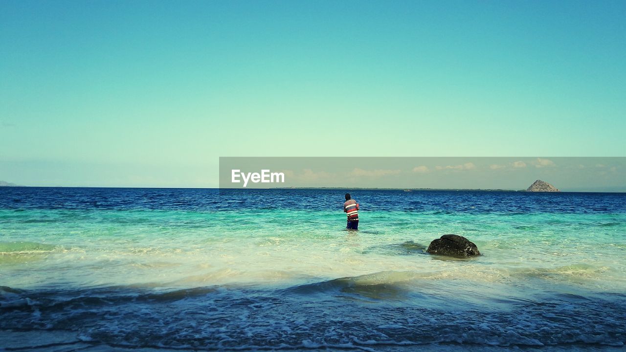 Rear view of man standing in sea against clear blue sky