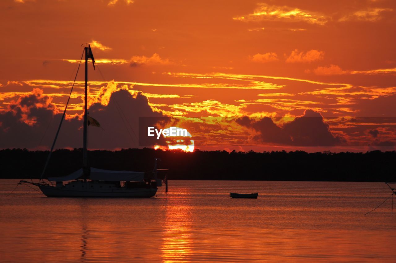 Silhouette sailboats in sea against orange sky