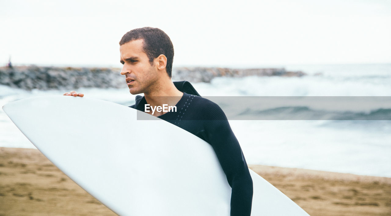 Portrait of surfer on beach against sky