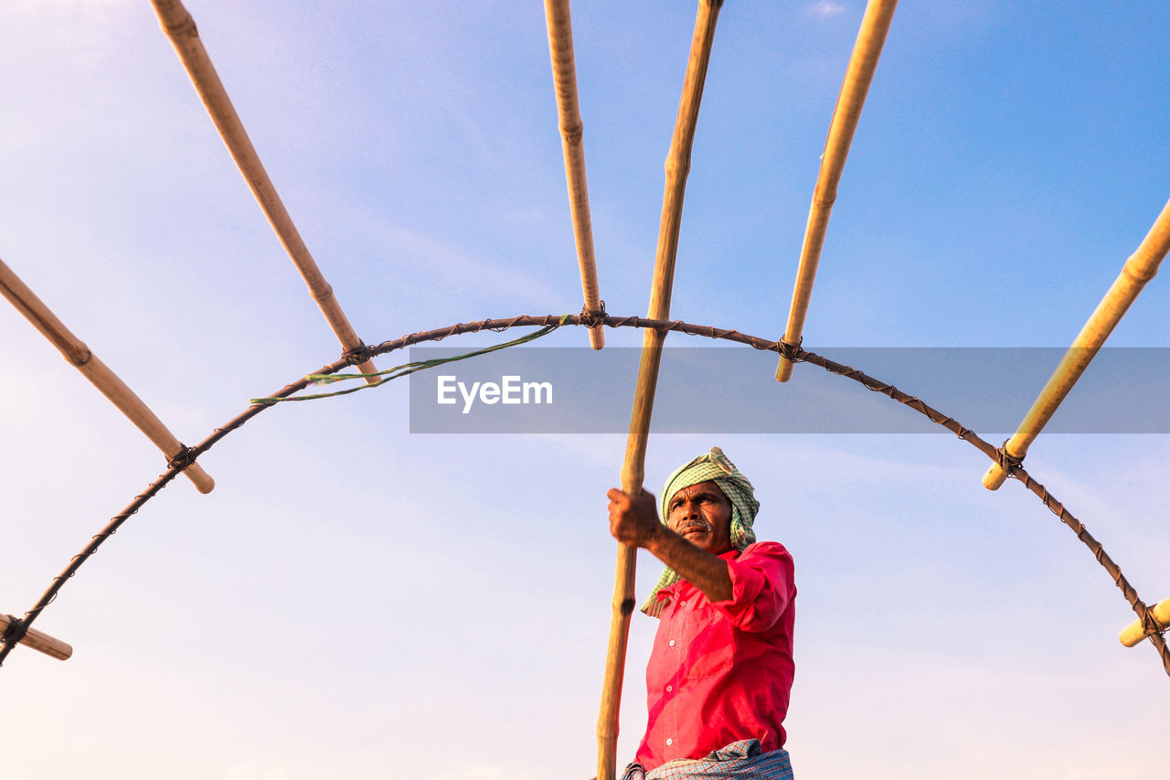 Low angle view of fisherman standing against sky during sunset