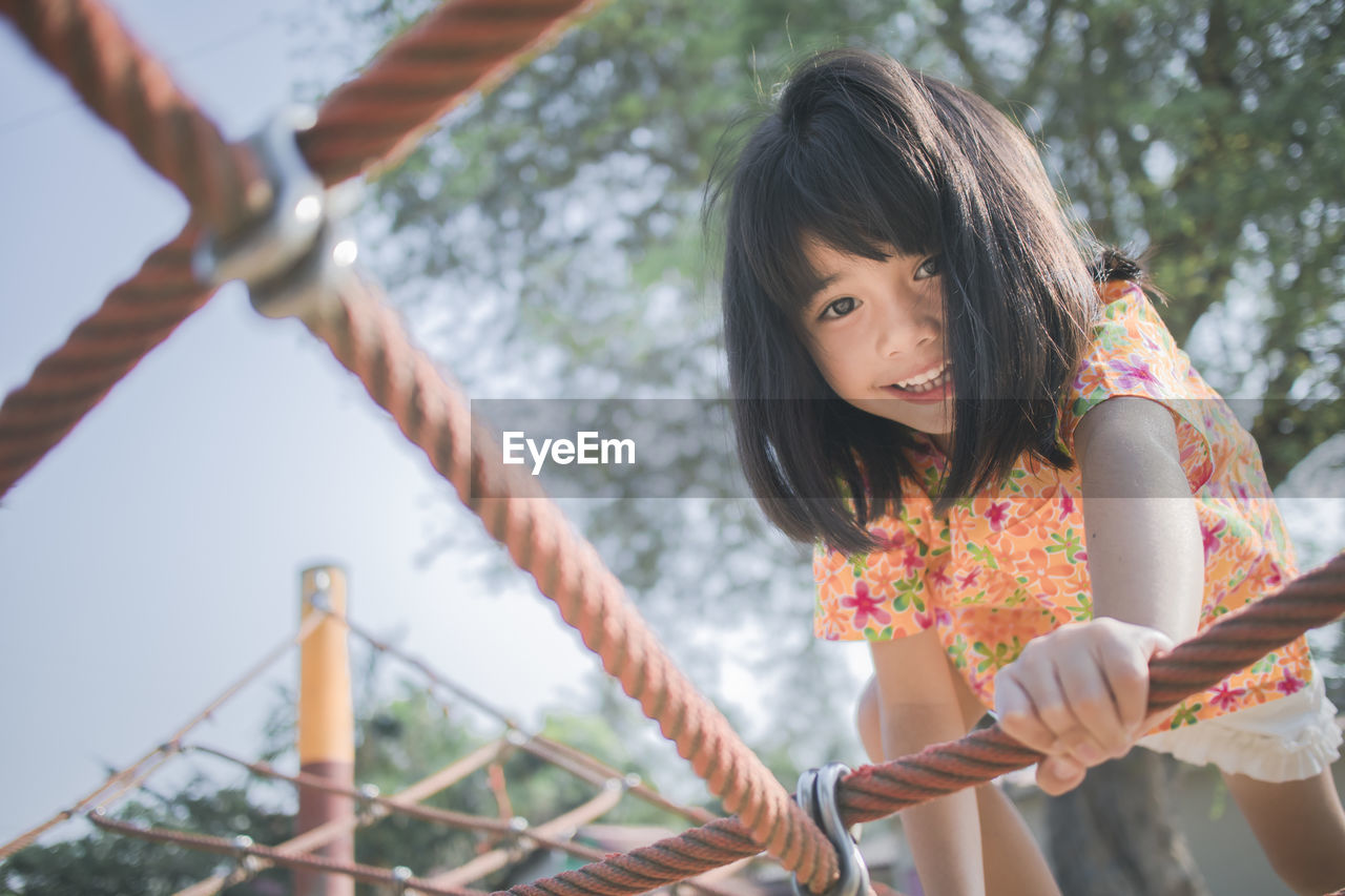 Low angle portrait of smiling girl climbing jungle gym in playground