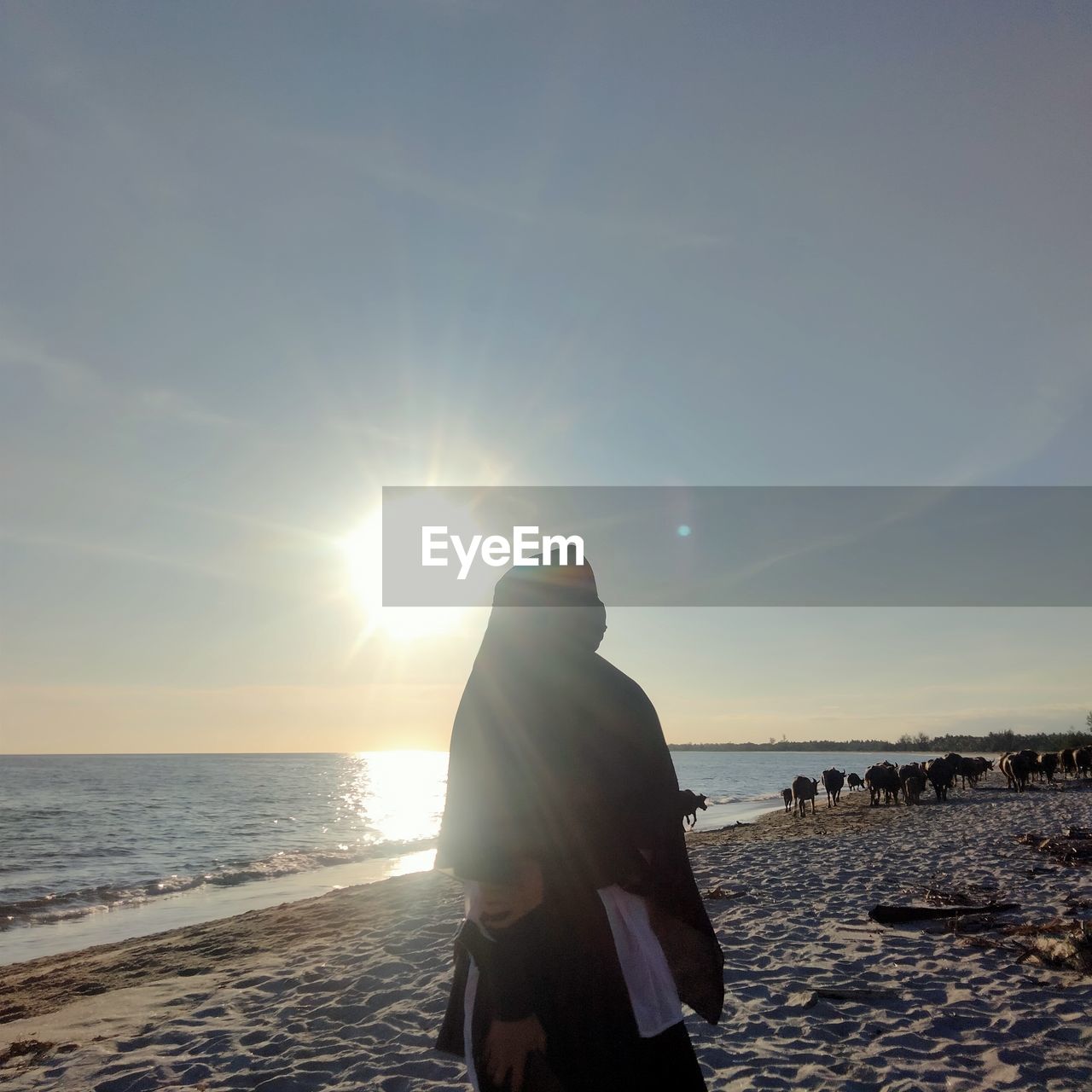WOMAN STANDING AT BEACH DURING SUNSET