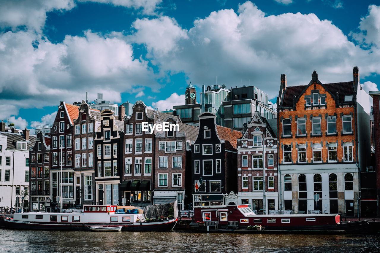 Boats on canal by buildings against cloudy sky in city