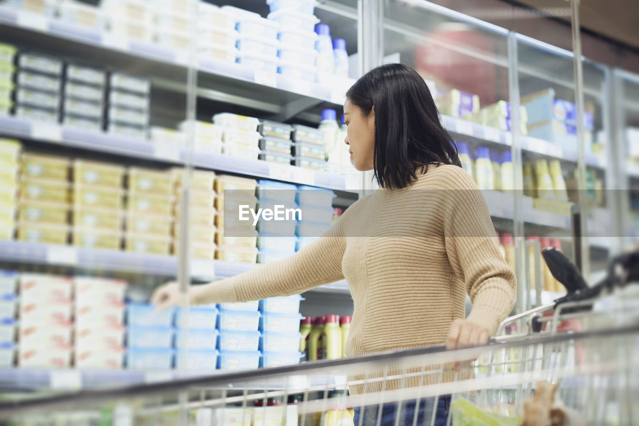 Woman in supermarket standing in front of fridge and choosing food