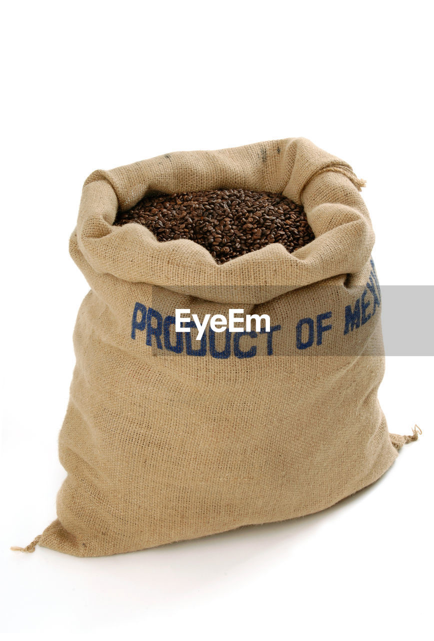 Close-up of roasted coffee beans in sack over white background