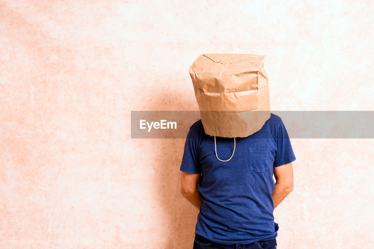 MIDSECTION OF A BOY HOLDING PAPER AGAINST WALL