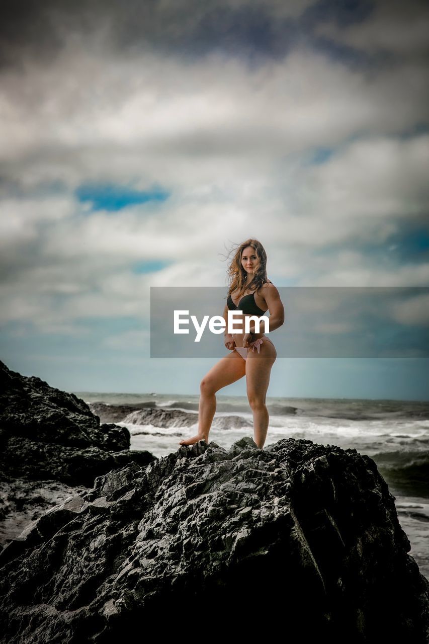 Full length of woman wearing bikini standing on rock at beach