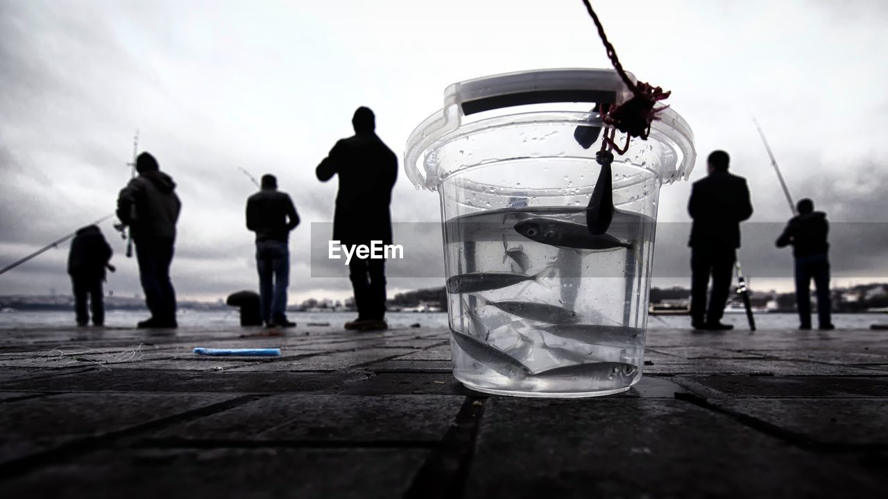Close-up of fish in jar with people in background at lake