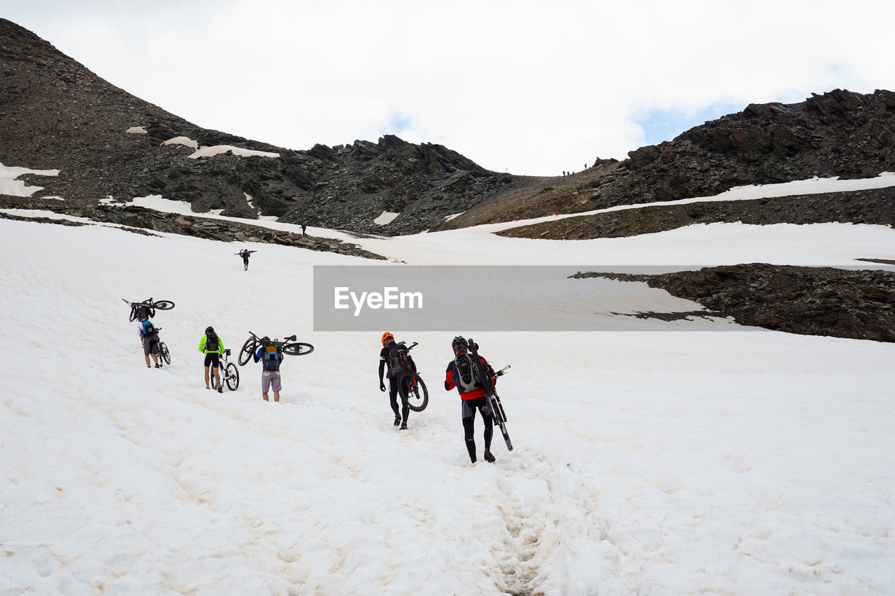 People carrying their mountain bikes on snowcapped mountain against sky