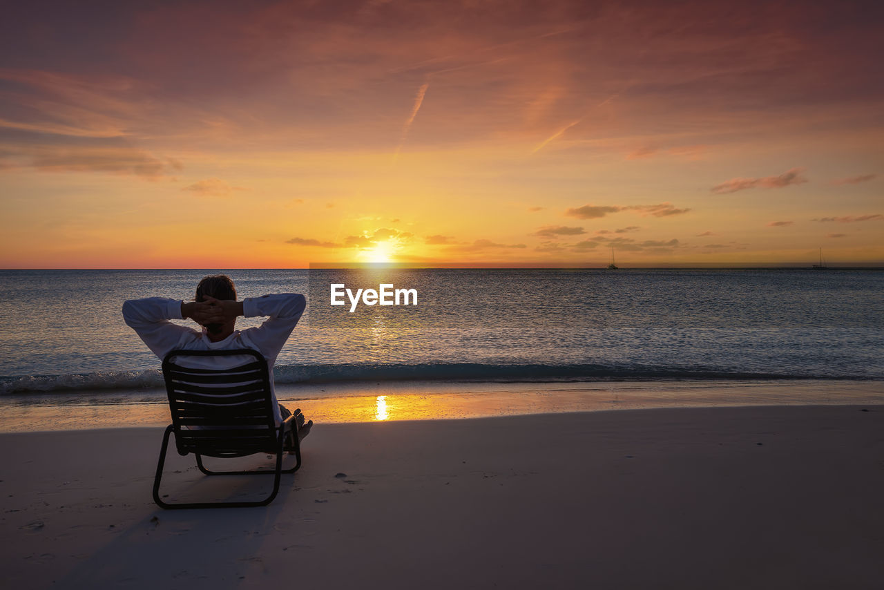 rear view of woman sitting on beach at sunset