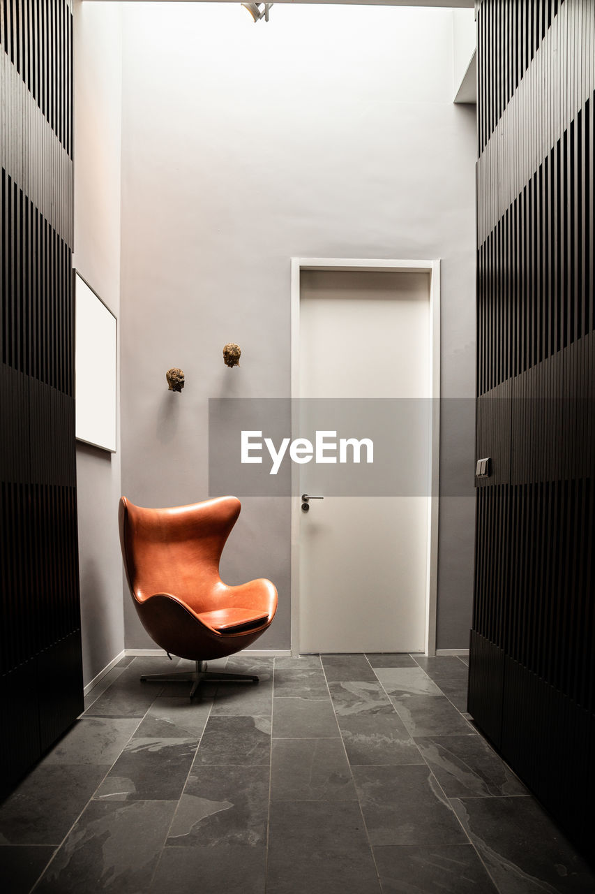 Perspective view of hallway interior with gray striped walls and brown chair placed near entry door