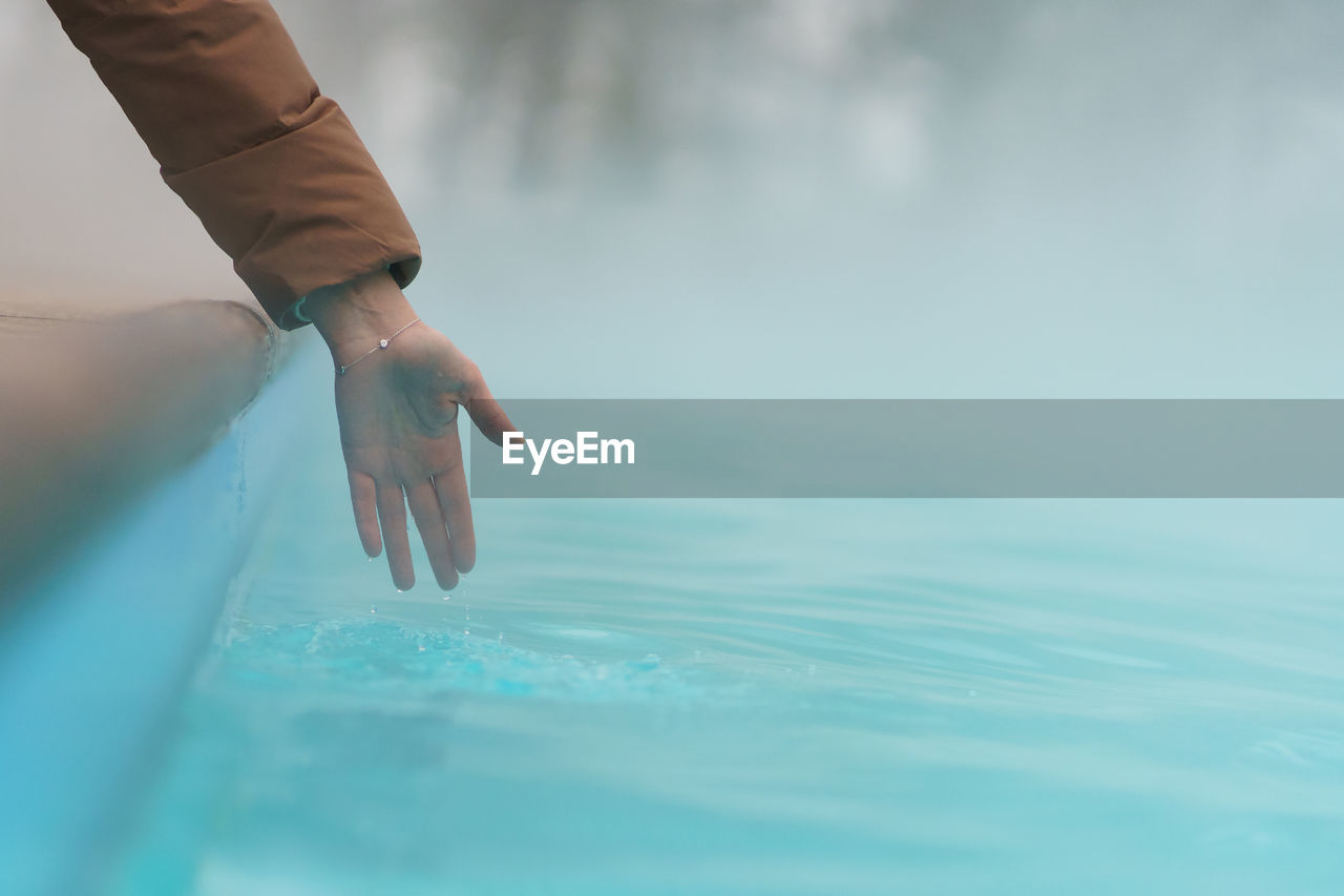 Hand of woman checking temperature of water in open swimming pool in winter. thermal spa outdoors.