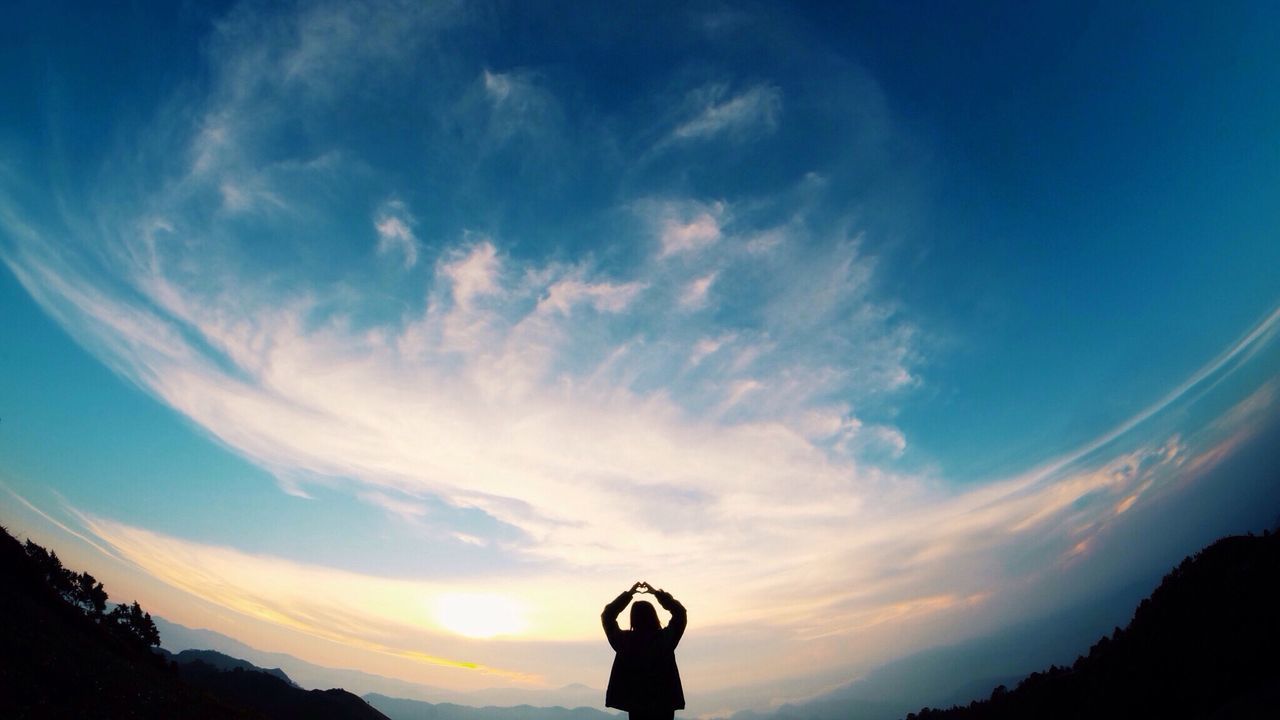 Silhouette person standing with arms raised against sky