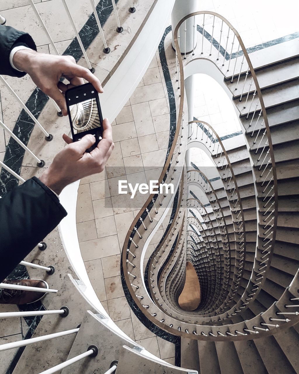 Cropped hands photographing spiral staircases using phone