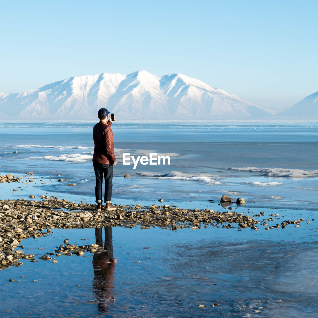 Rear view of man standing on shore against mountains