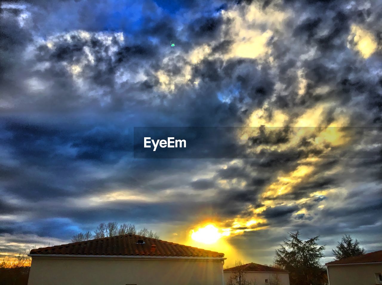 Low angle view of cloudy sky over houses during sunset