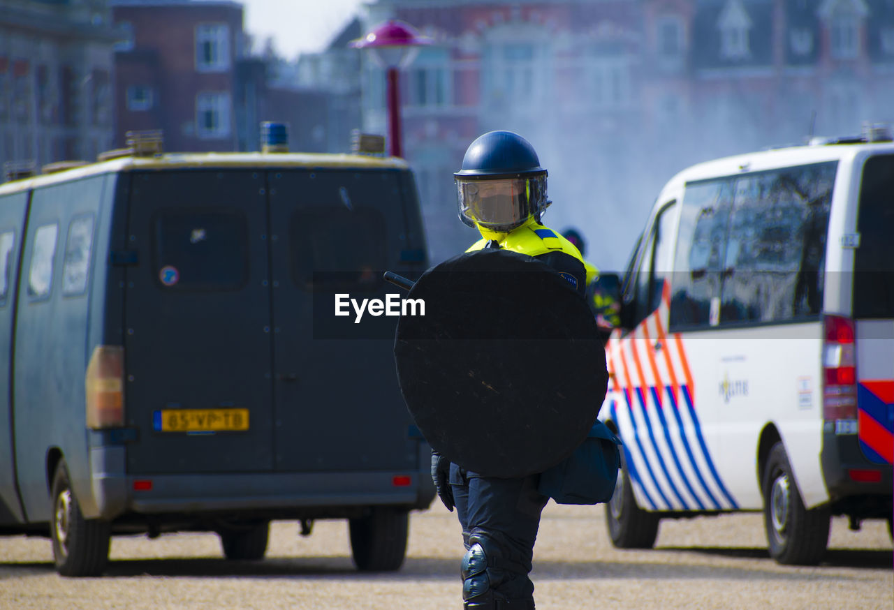 REAR VIEW OF MAN STANDING ON STREET AGAINST CITY