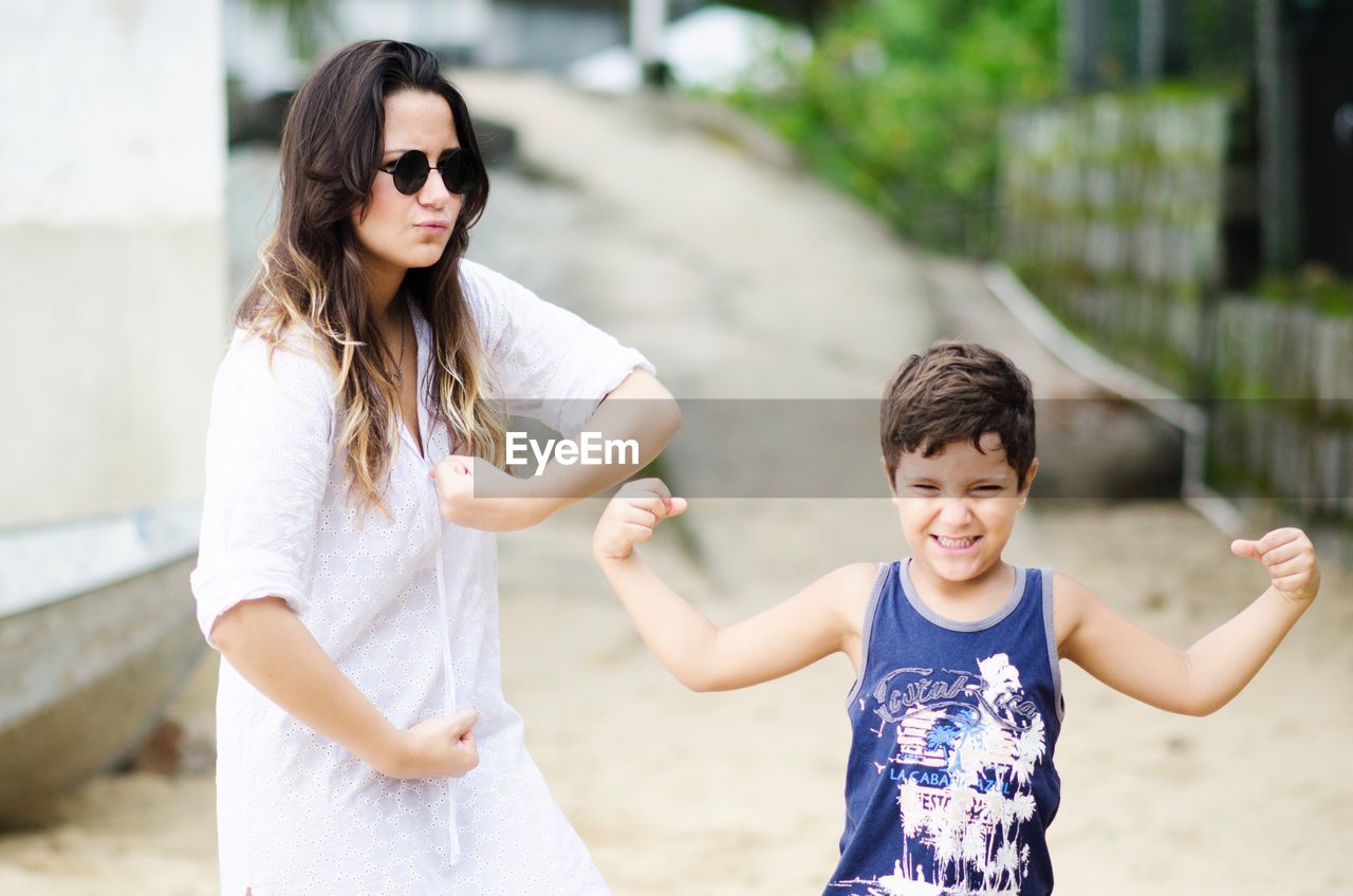Happy mother with son flexing muscles while standing on street