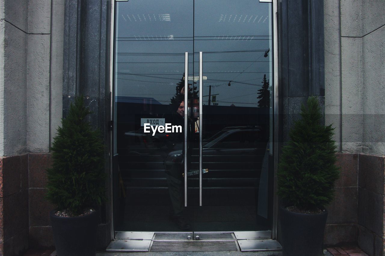 Full length of man seen through closed glass doors with reflection