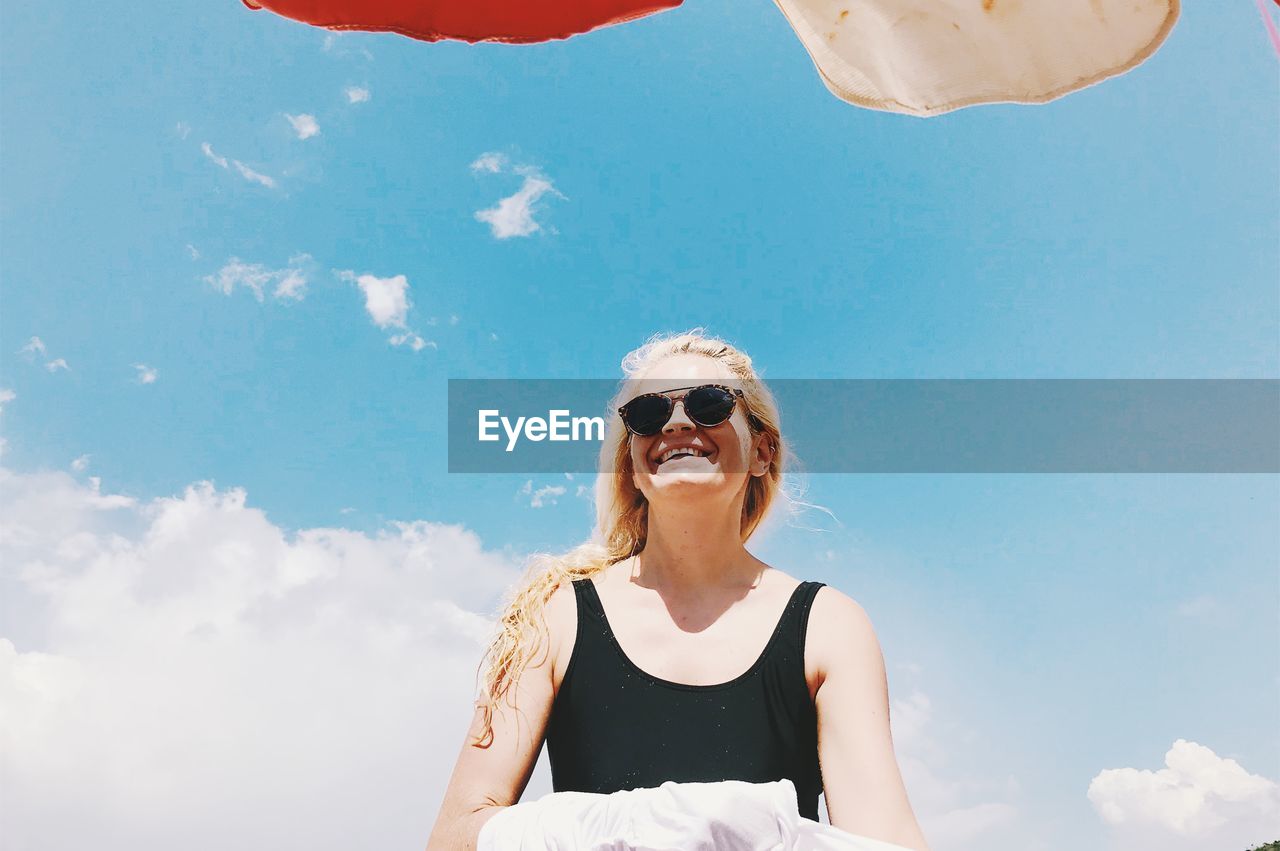 Cheerful woman wearing sunglasses standing against sky during sunny day
