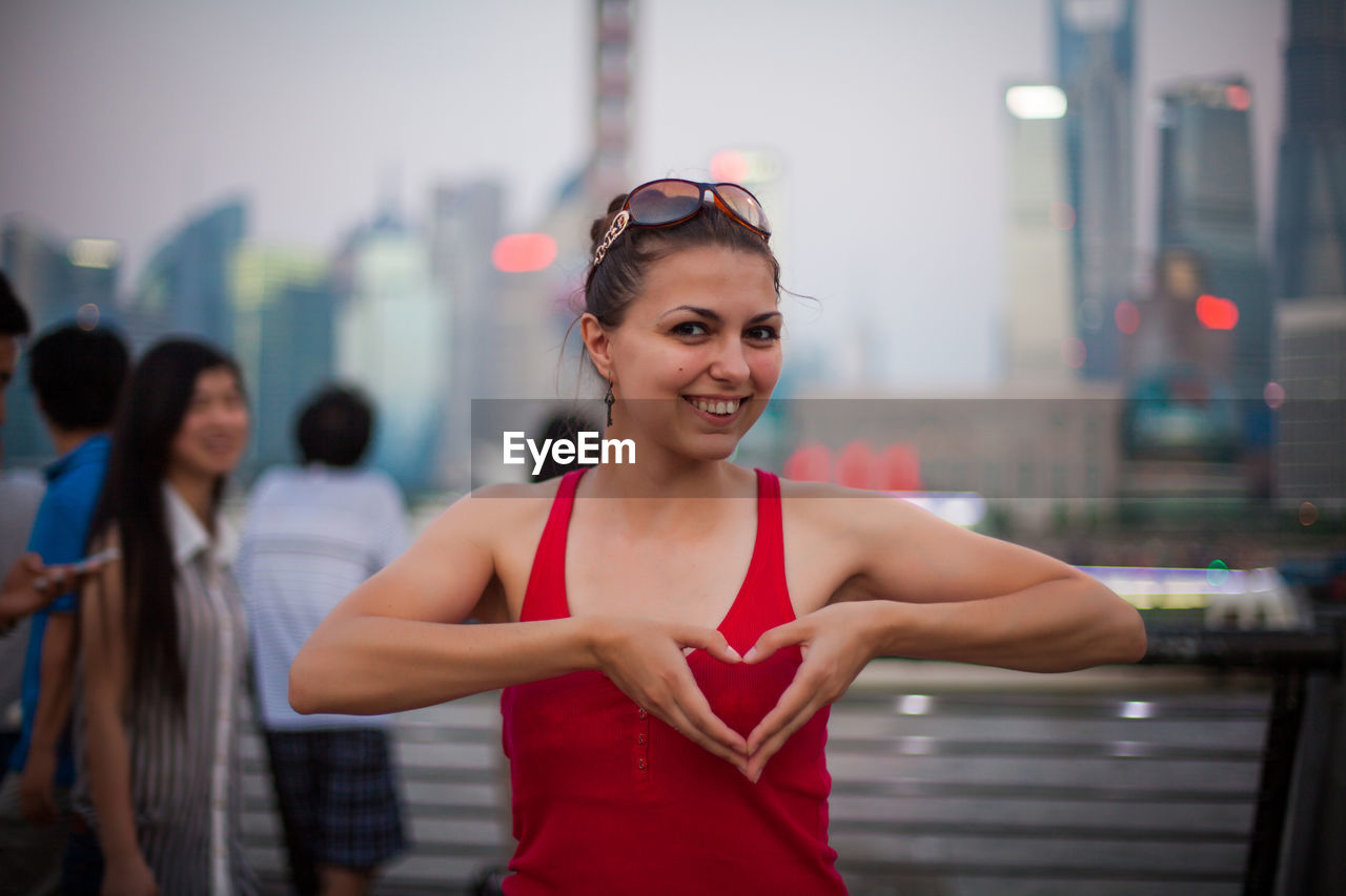 Portrait of happy woman making heart shape with hands in city