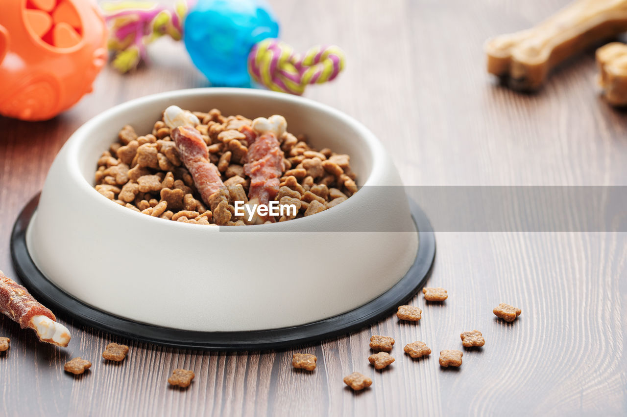 A bowl with dog food, dog treats and toys on a wooden floor. concept of healthy food for dogs.