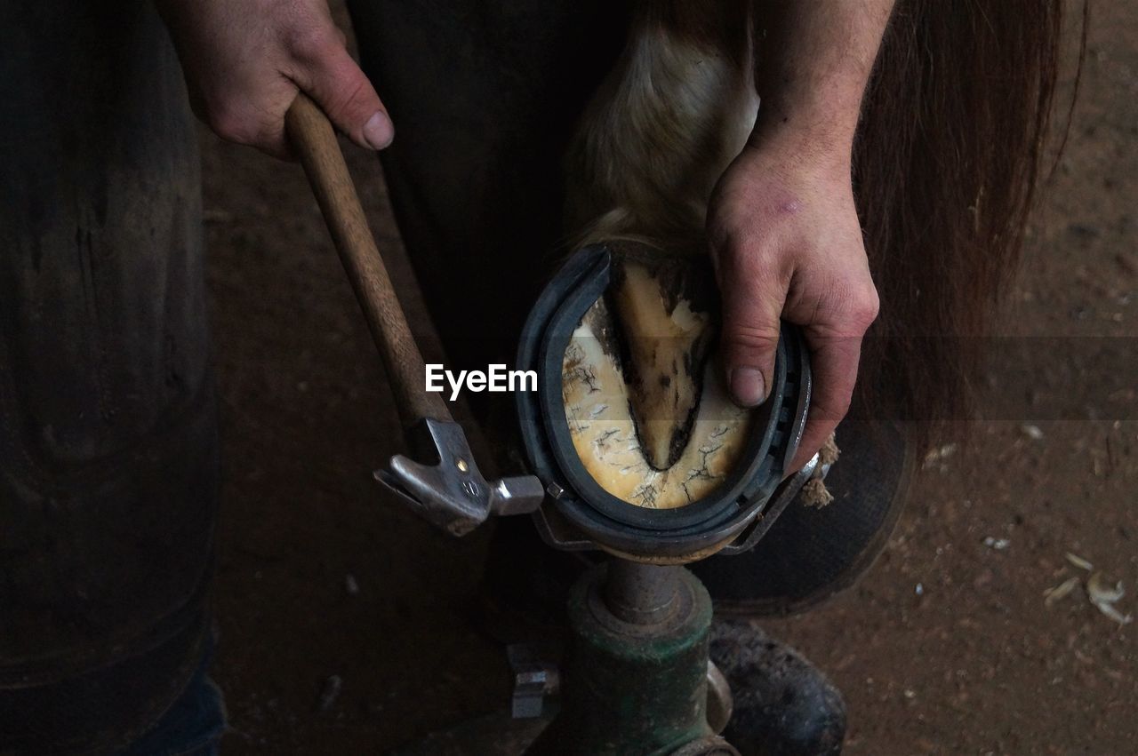 Cropped image of farrier hammering horseshoe in workshop