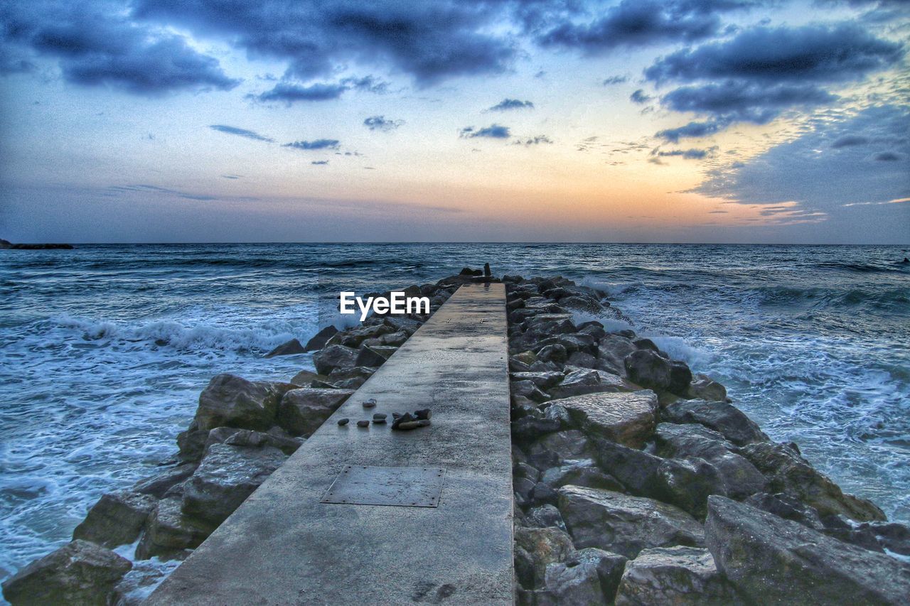 Pier amidst groyne against sky during sunset