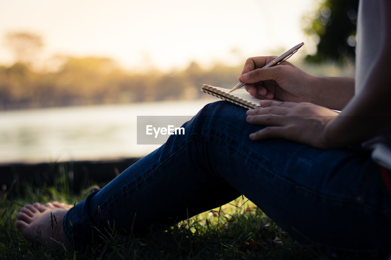 Low section of woman writing in book while sitting at park