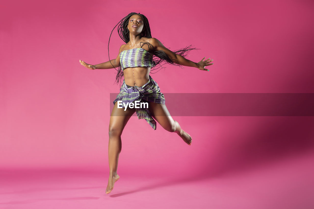 Portrait of young woman dancing against pink background