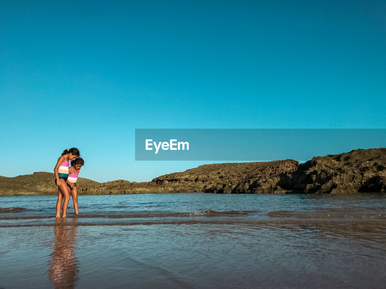 Girls standing on beach against clear sky