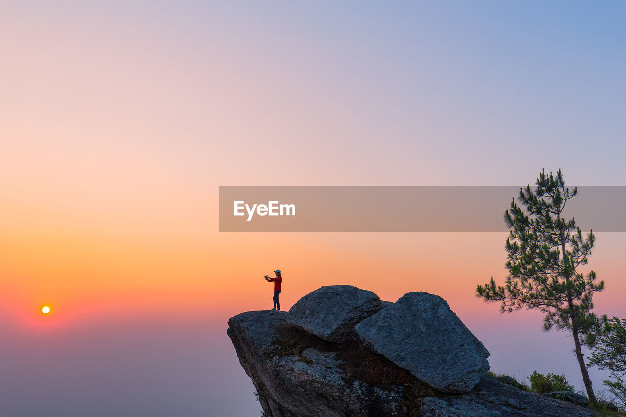 Person standing on rock against sky during sunset