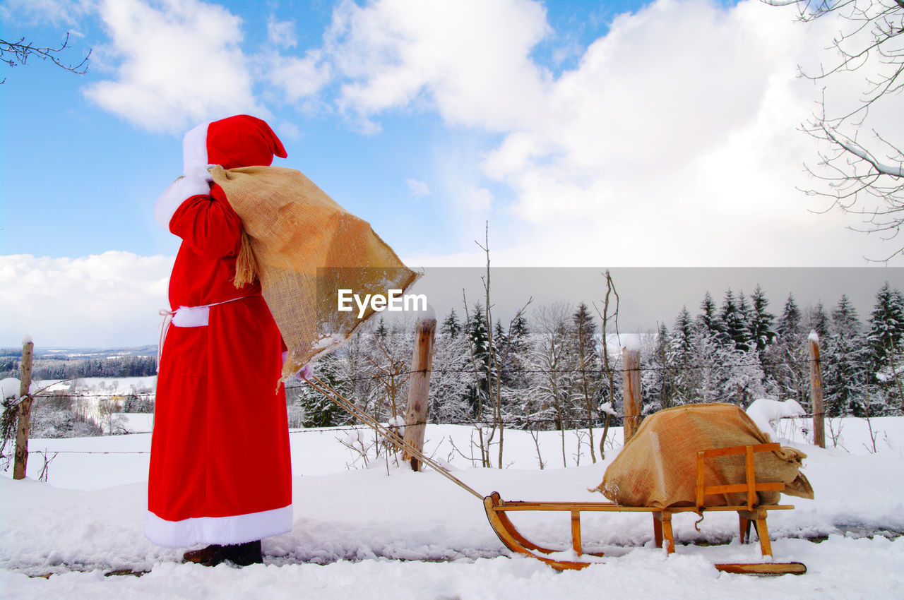 Side view of santa claus pulling sled on snow against sky