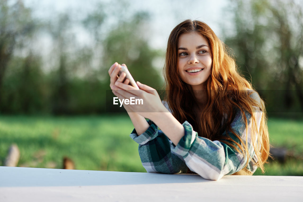 young woman using mobile phone while sitting outdoors