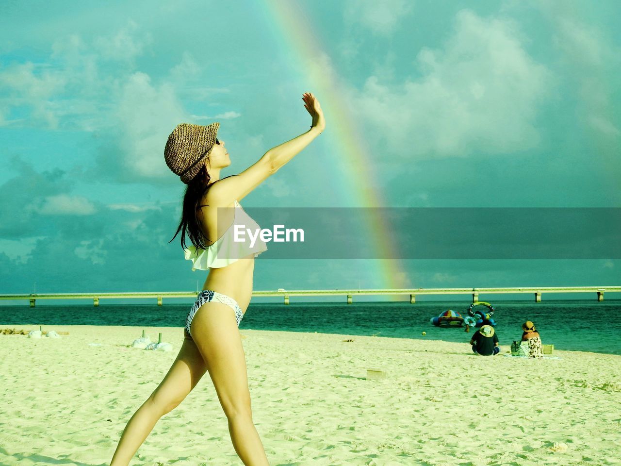 Side view of woman standing against rainbow at beach