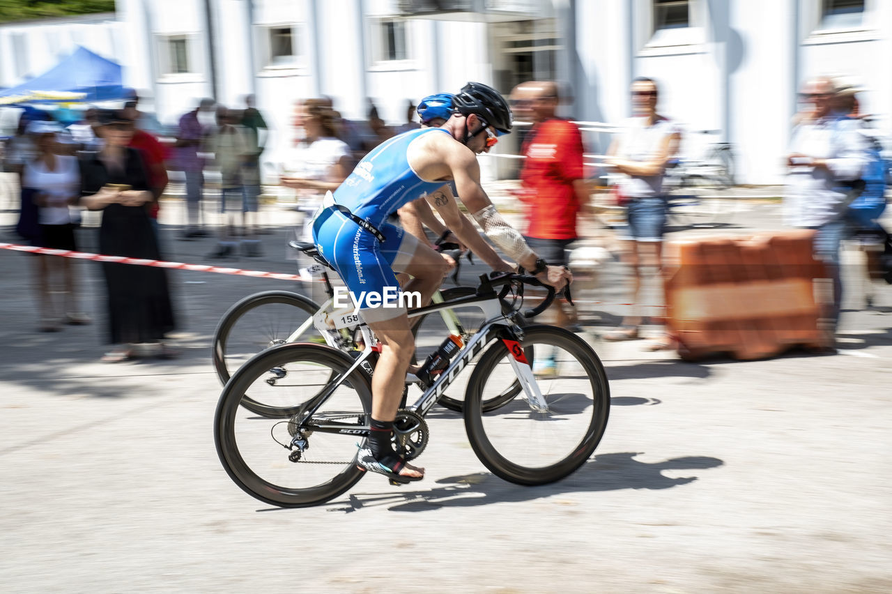 bicycle, transportation, motion, sports, activity, blurred motion, cycling, city, architecture, road cycling, adult, endurance sports, city life, vehicle, lifestyles, street, mode of transportation, road bicycle, men, speed, sports equipment, city street, riding, cycle sport, bicycle racing, group of people, building exterior, commuter, clothing, full length, racing bicycle, wheel, road bicycle racing, built structure, race, on the move, person, exercising, bicycle wheel, travel, footwear, road, helmet, women, outdoors, headwear, competition, bicycle helmet, crowd
