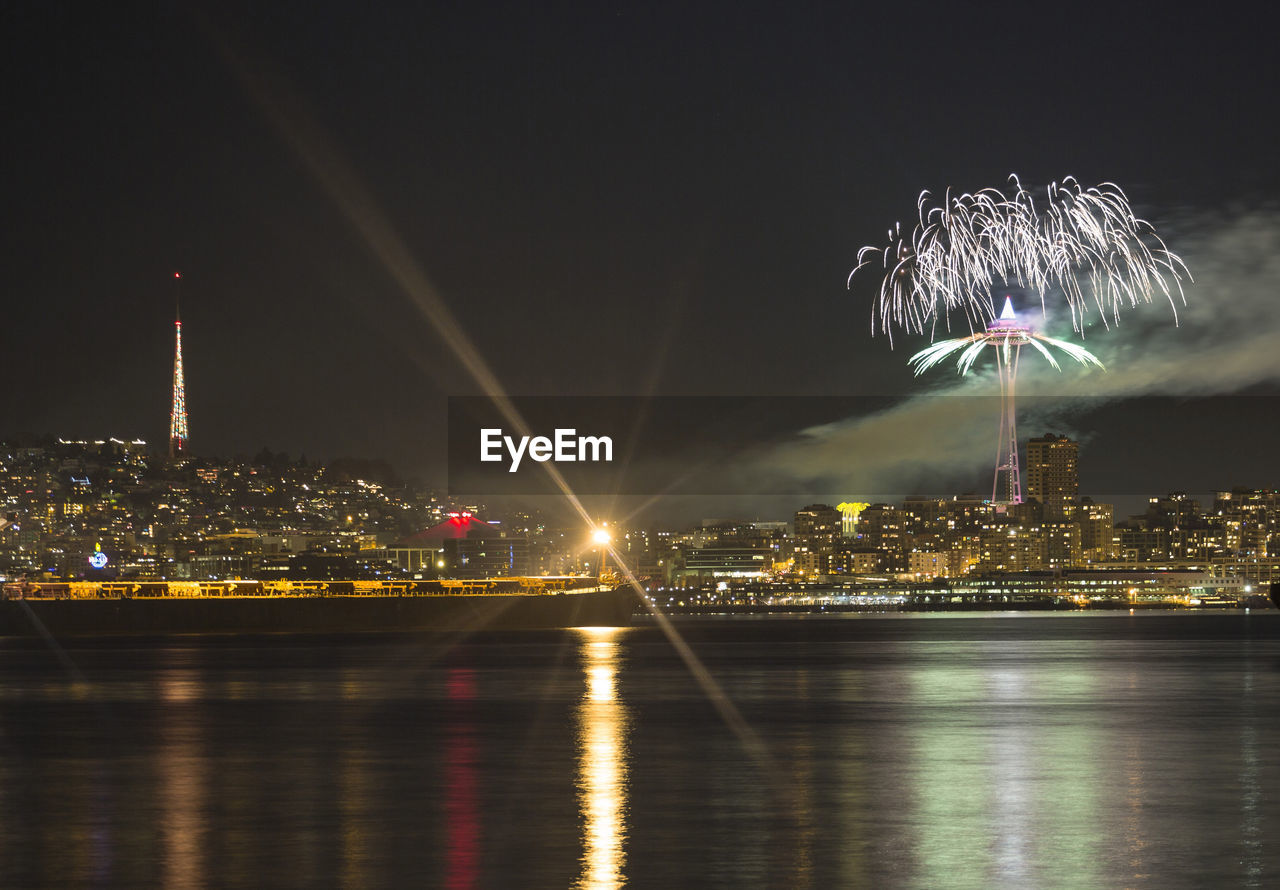 FIREWORK DISPLAY OVER RIVER AND ILLUMINATED BUILDINGS IN CITY