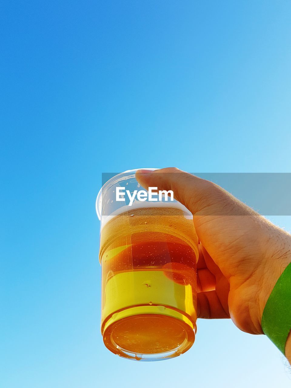 Cropped hand holding beer against clear blue sky