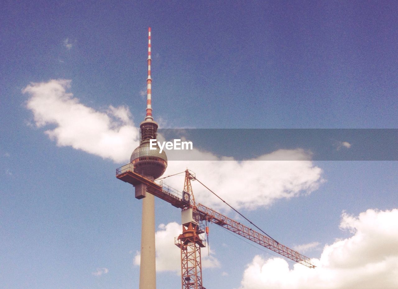 Low angle view of crane by fernsehturm against sky