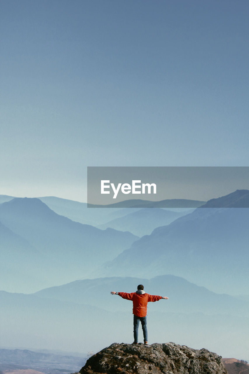 Rear view of man standing on mountain against sky