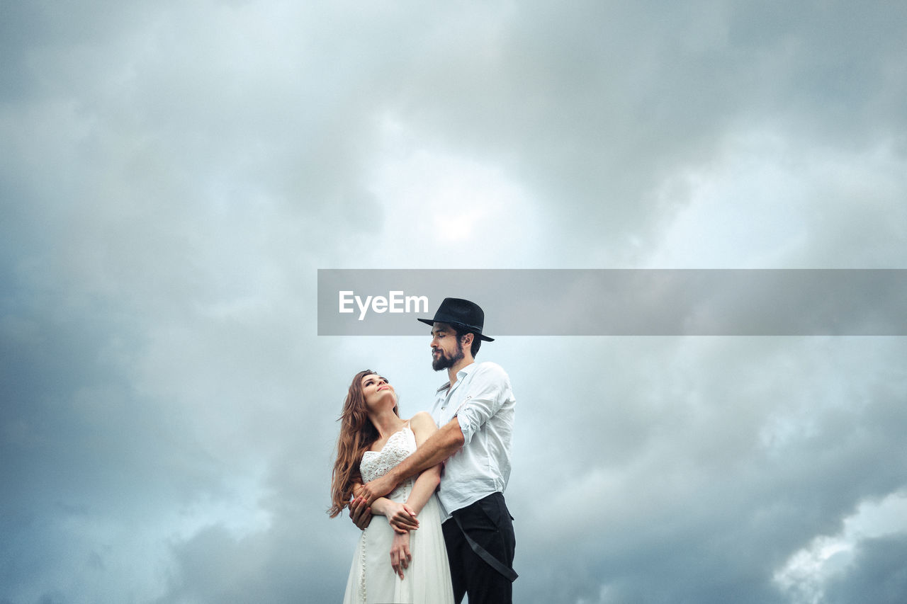 Low angle view of man embracing woman while standing against cloudy sky