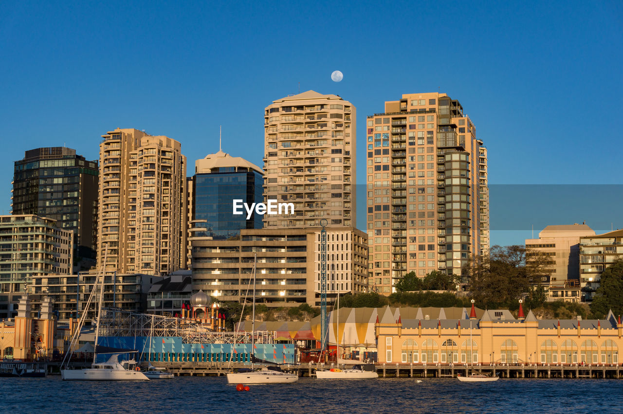 Modern buildings by river against blue sky