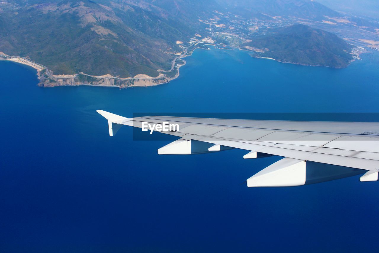 Cropped image airplane wing flying over sea