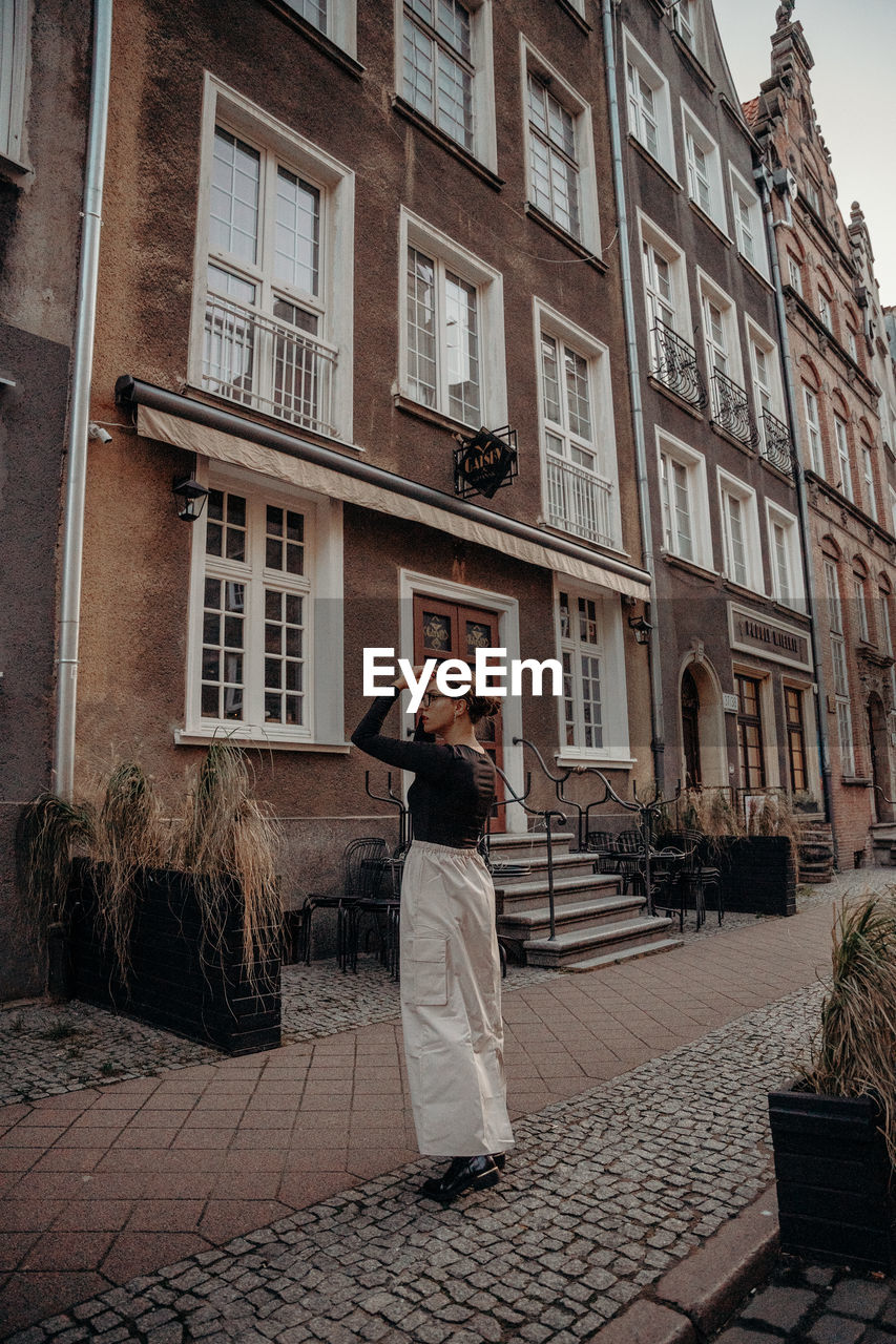 architecture, building exterior, built structure, city, one person, street, adult, full length, road, building, urban area, cobblestone, women, window, lifestyles, wall, standing, footpath, day, rear view, leisure activity, clothing, outdoors, nature, house, photographing, person, men, young adult, residential district, casual clothing, city life, technology